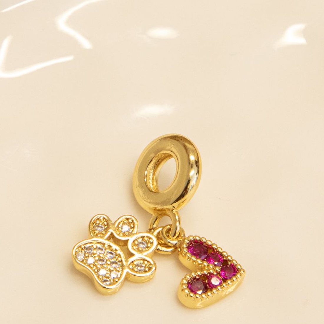 Gold charms on a white dish: a crystal paw print and a heart set with pink stones.