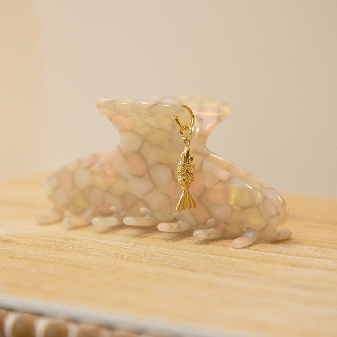 A blush and cream marbled claw clip finished with a textured gold fish charm with a tiny red eye.