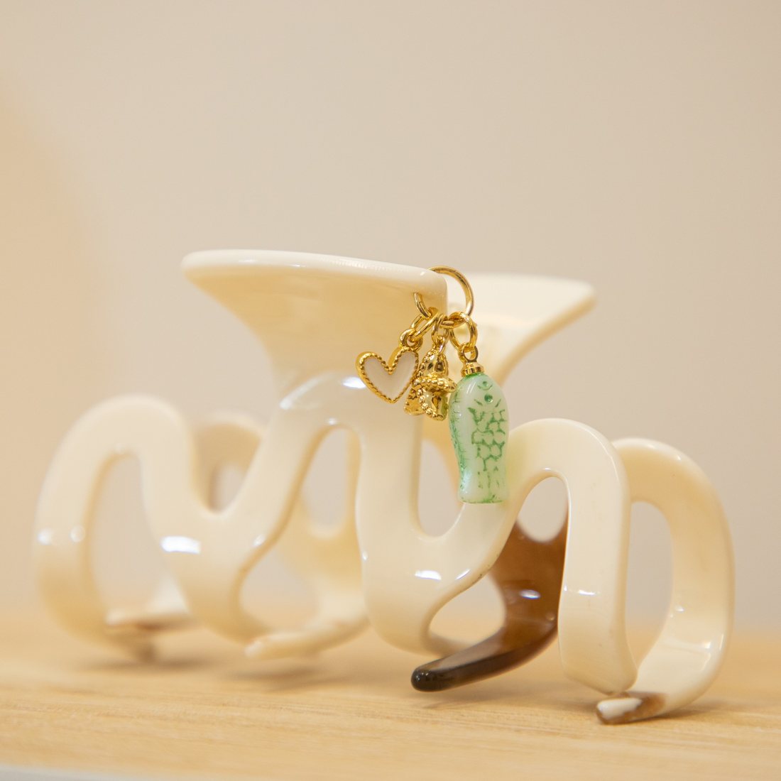 A cream wavy claw clip finished with a gold heart charm, a gold starfish and a mint green fish charm.
