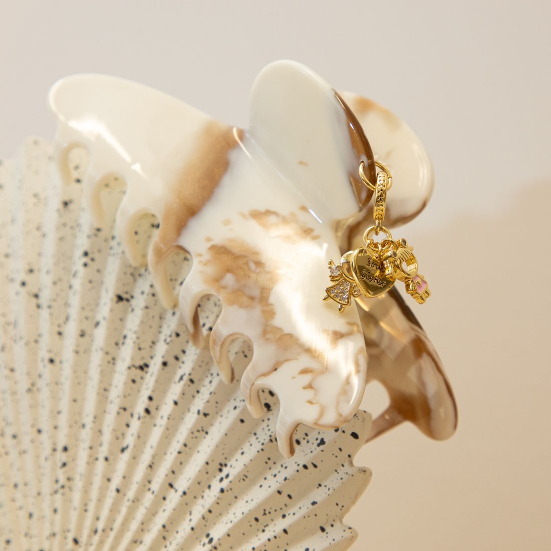 A cream and caramel marbled claw clip finished with gold charms: two little girls and a Soul Sister heart.
