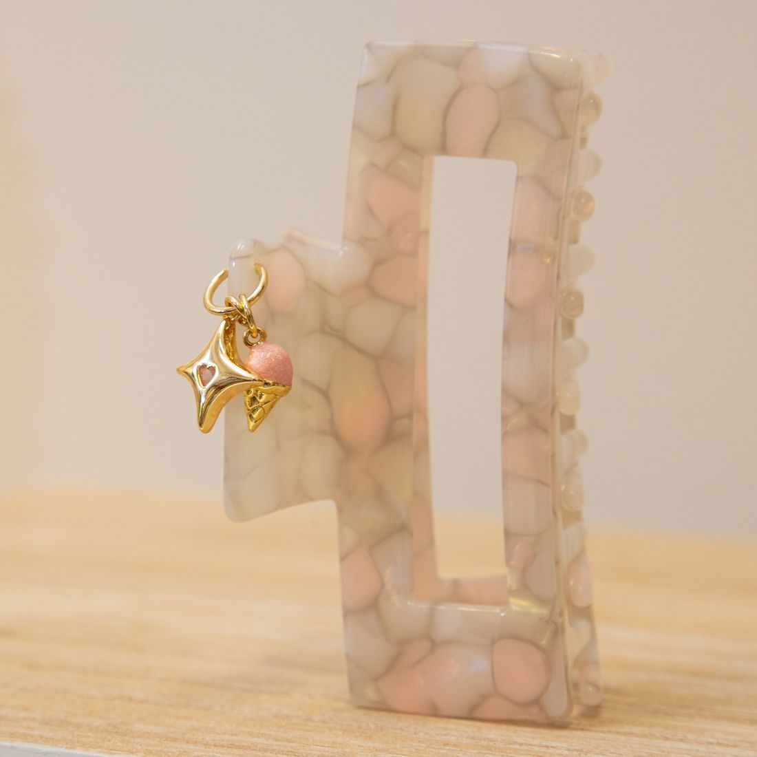A rectangular blush and cream claw clip finished with a gold star charm and a pink ice cream charm.