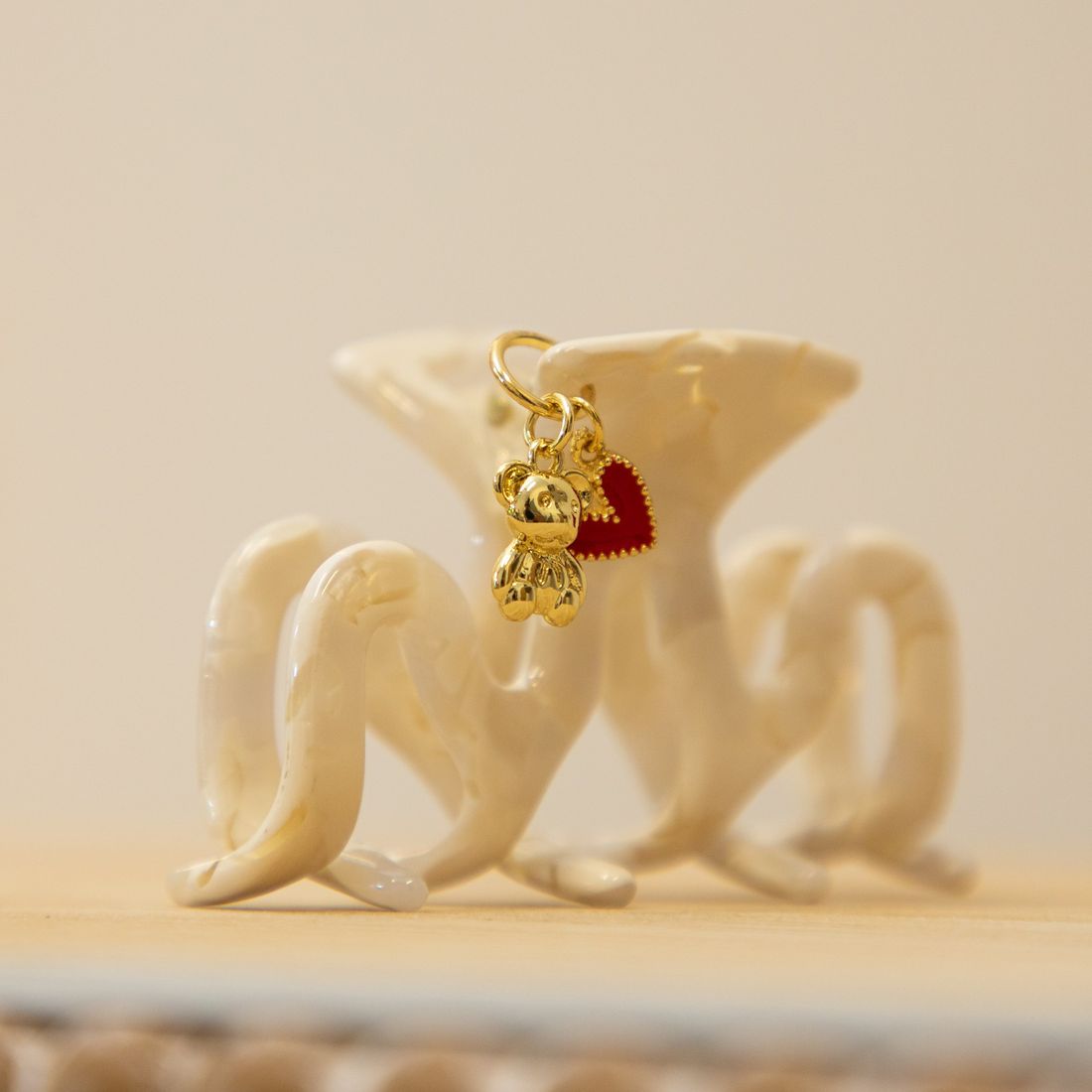A cream marbled claw clip finished with a gold teddy bear charm and a red heart charm.