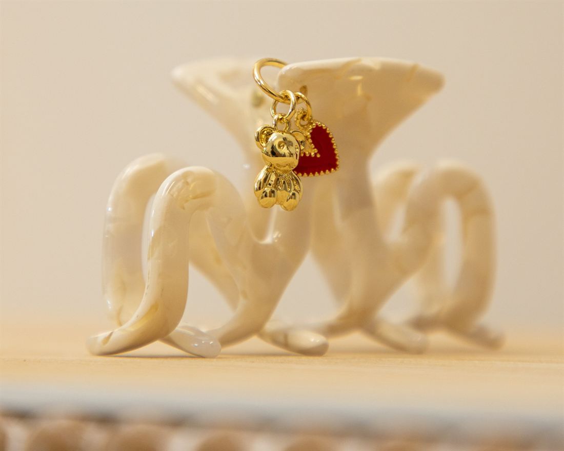 This month's claw clip: a cream marbled claw clip finished with a gold teddy bear charm and a red heart charm.