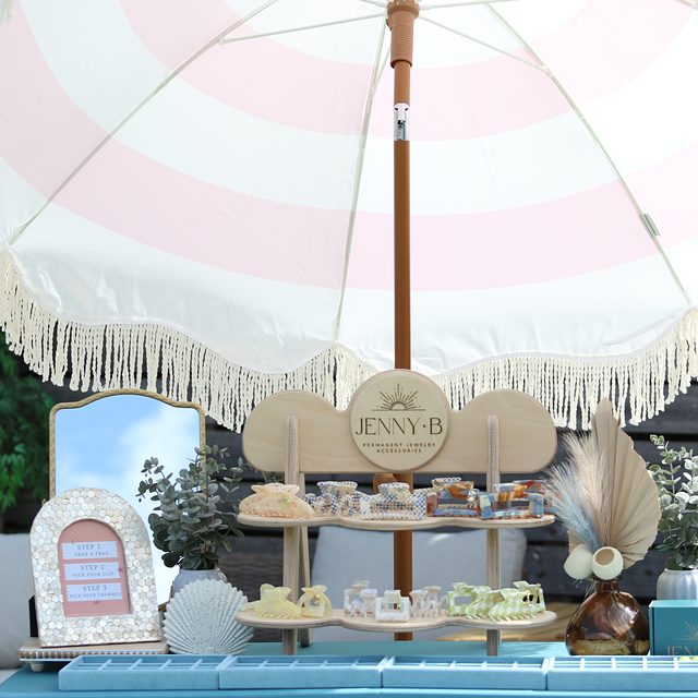 The Jenny B charm stand and arched mirror under a pink and white striped fringe umbrella.