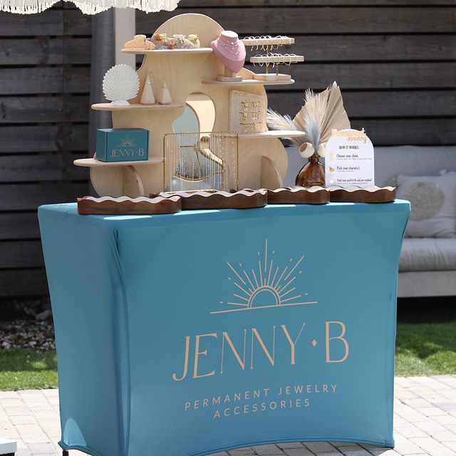 The teal Jenny B table with a wooden display of chains, charms and necklaces.