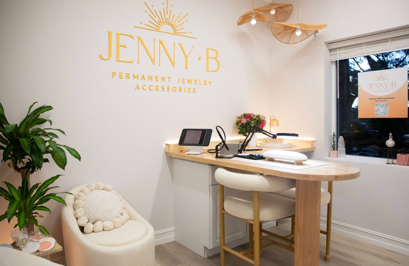 The Jenny B studio: the gold sun logo on the wall, a curved wooden welding table with boucle stools, rattan pendant lights and a window.